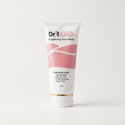 A 100 ml squeeze tube of Dr RAMZI Brightening Face Wash, featuring a white and pink design with a gold accent band near the cap, set against a plain light gray background.